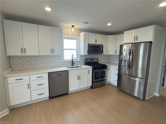 kitchen featuring white cabinets, light wood-style flooring, stainless steel appliances, light countertops, and a sink