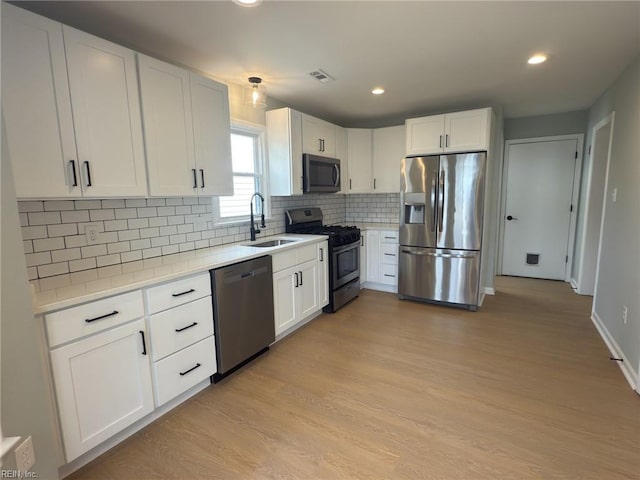 kitchen with light wood finished floors, light countertops, appliances with stainless steel finishes, white cabinets, and a sink