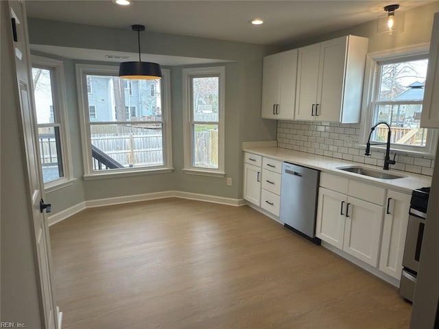 kitchen with stainless steel appliances, a sink, white cabinets, light countertops, and decorative backsplash