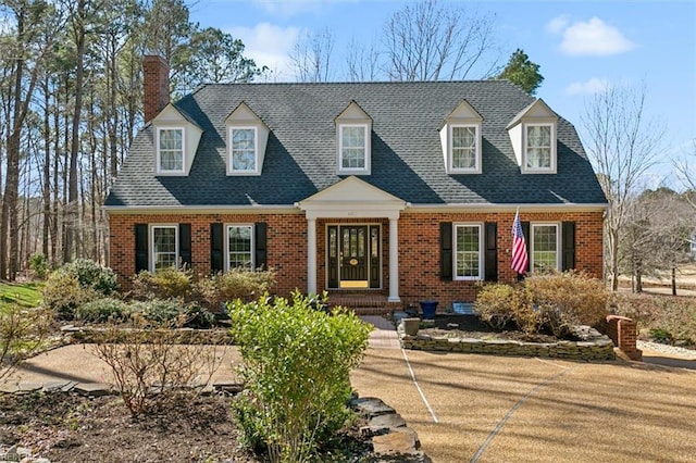 new england style home featuring brick siding and roof with shingles