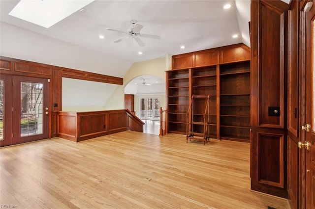 unfurnished living room featuring arched walkways, recessed lighting, a ceiling fan, light wood-type flooring, and lofted ceiling with skylight