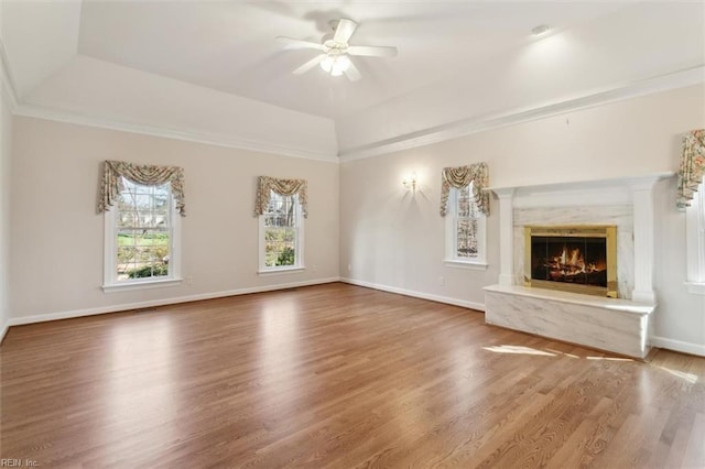 unfurnished living room with a high end fireplace, a tray ceiling, a ceiling fan, and wood finished floors