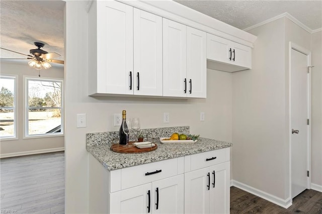 kitchen featuring a textured ceiling, light stone counters, white cabinetry, baseboards, and dark wood-style floors