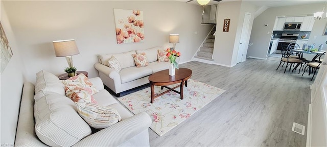 living room with light wood-style floors, baseboards, and stairs