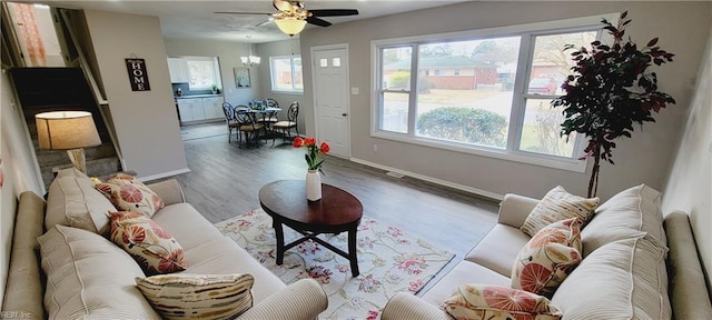 living room featuring ceiling fan with notable chandelier, wood finished floors, and baseboards