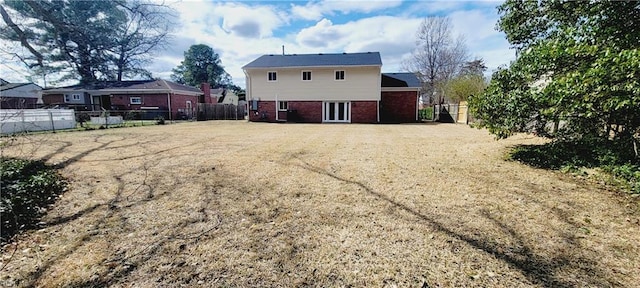 rear view of house featuring a fenced backyard, a lawn, and brick siding