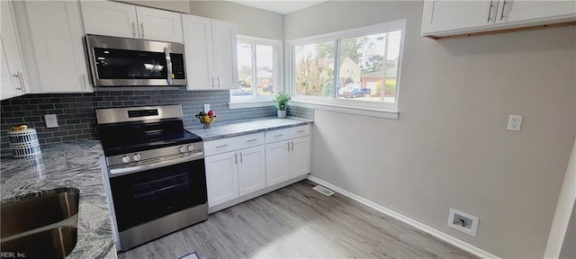 kitchen featuring light stone countertops, appliances with stainless steel finishes, white cabinets, and backsplash