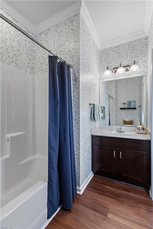 bathroom with wallpapered walls, shower / tub combo with curtain, wood finished floors, crown molding, and vanity