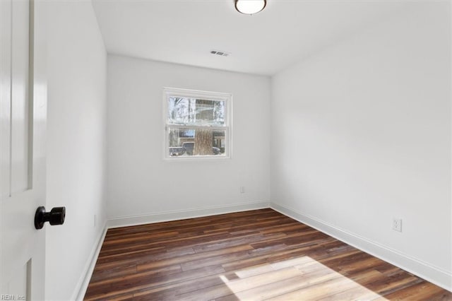 spare room with dark wood-style flooring, visible vents, and baseboards