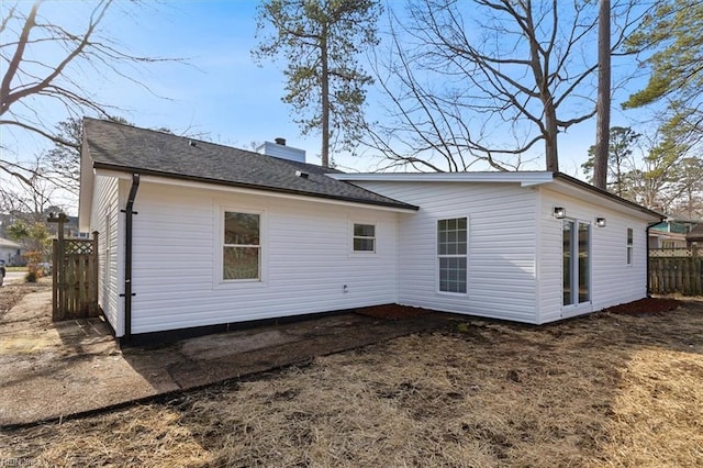 rear view of property featuring a shingled roof, a chimney, and fence