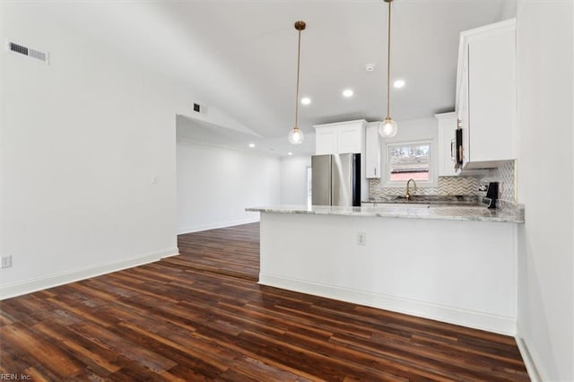 kitchen featuring lofted ceiling, a peninsula, appliances with stainless steel finishes, decorative backsplash, and dark wood-style floors