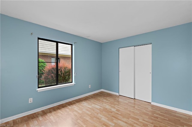 unfurnished bedroom featuring light wood finished floors, baseboards, and a closet