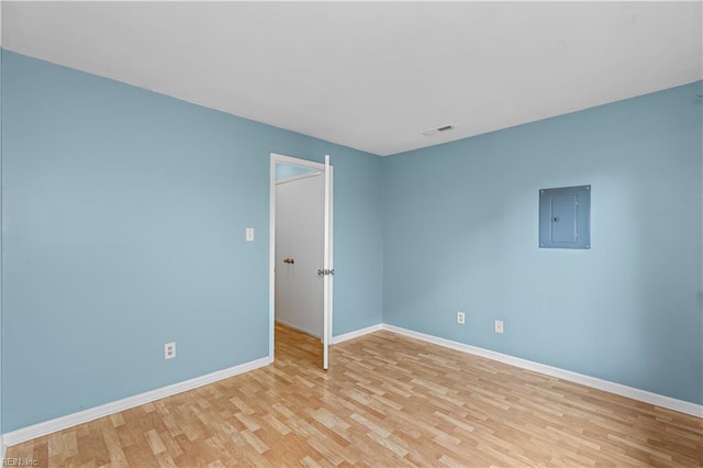 unfurnished room with light wood-type flooring, electric panel, visible vents, and baseboards