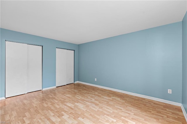 unfurnished bedroom with light wood-type flooring, baseboards, and two closets