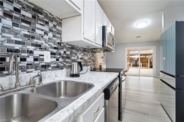 kitchen featuring tasteful backsplash, white cabinets, stainless steel appliances, a textured ceiling, and a sink