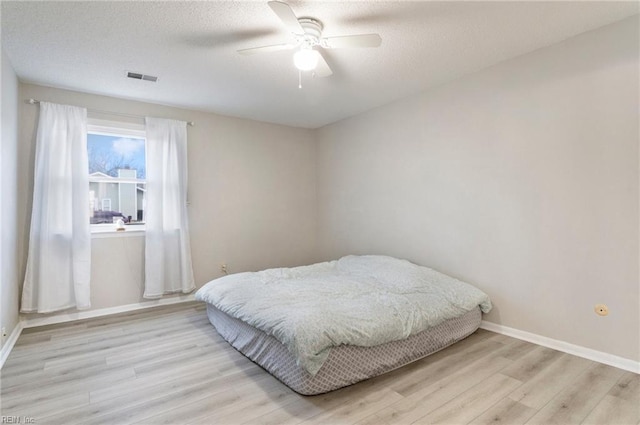 bedroom with visible vents, a textured ceiling, baseboards, and wood finished floors