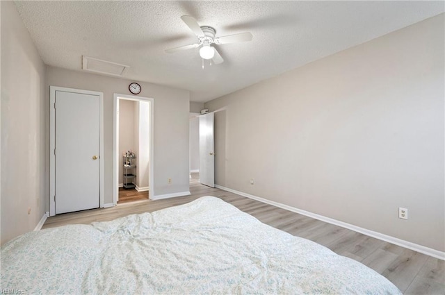 bedroom featuring a textured ceiling, wood finished floors, a ceiling fan, baseboards, and attic access