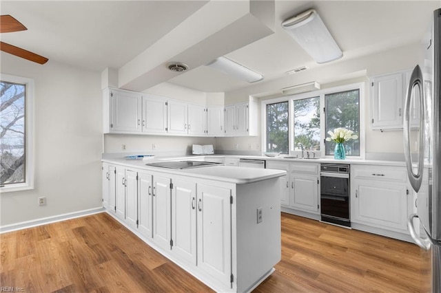 kitchen with stainless steel appliances, light countertops, white cabinetry, a sink, and light wood-type flooring