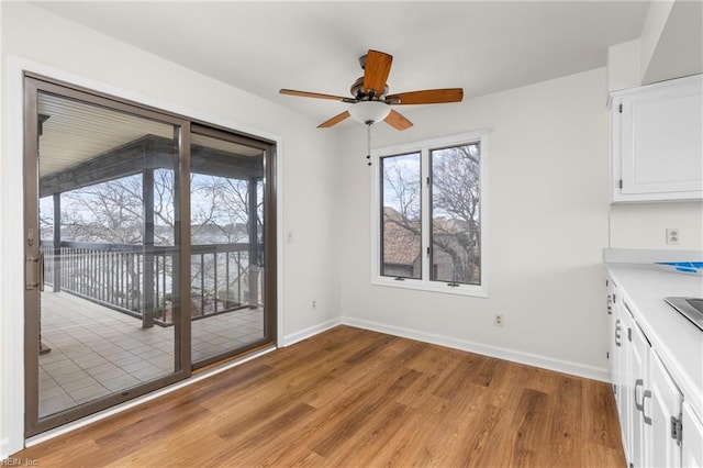 unfurnished dining area featuring light wood-type flooring, a ceiling fan, and baseboards