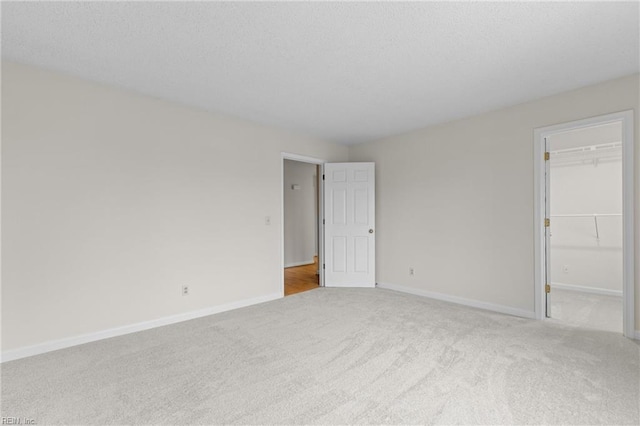 unfurnished bedroom featuring carpet floors, a spacious closet, baseboards, and a textured ceiling