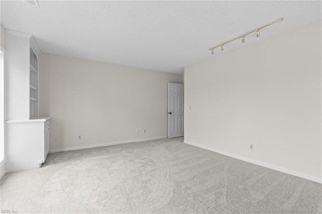 unfurnished room featuring track lighting, light carpet, a textured ceiling, and baseboards