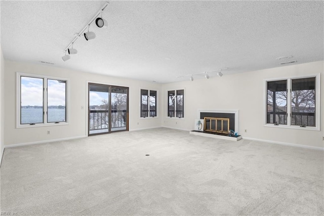 unfurnished living room with a textured ceiling, carpet floors, a glass covered fireplace, and baseboards