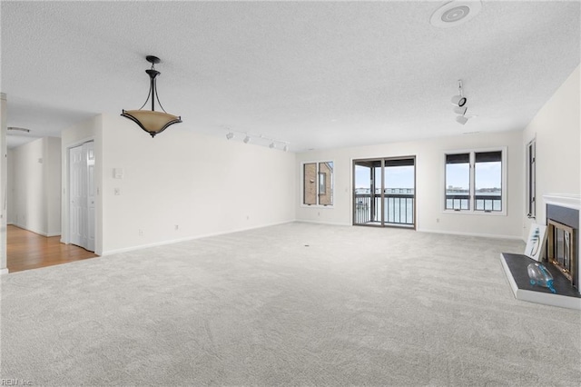 unfurnished living room featuring track lighting, carpet, a textured ceiling, and baseboards