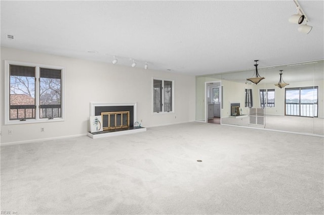 unfurnished living room featuring carpet, a glass covered fireplace, rail lighting, and baseboards