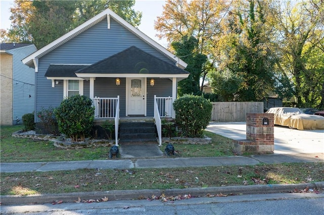 bungalow-style house featuring covered porch, fence, and roof with shingles