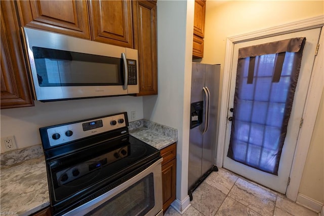 kitchen with appliances with stainless steel finishes, light stone counters, and brown cabinets