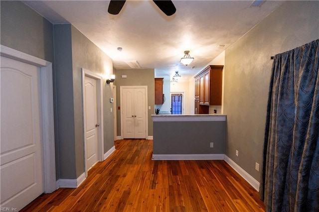 kitchen featuring dark wood-style flooring, brown cabinetry, a ceiling fan, a peninsula, and baseboards