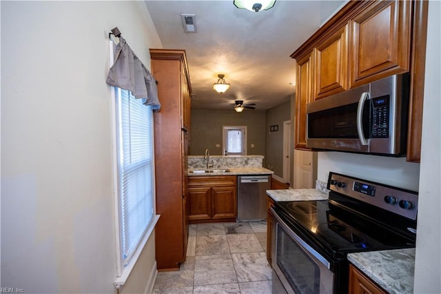 kitchen featuring stainless steel appliances, brown cabinetry, a sink, and light stone counters