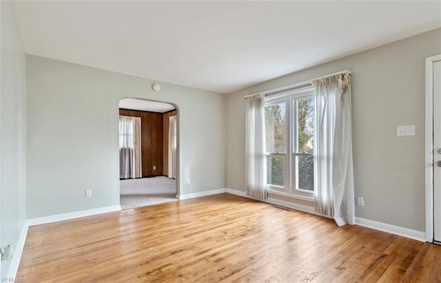 spare room with arched walkways, baseboards, and wood finished floors