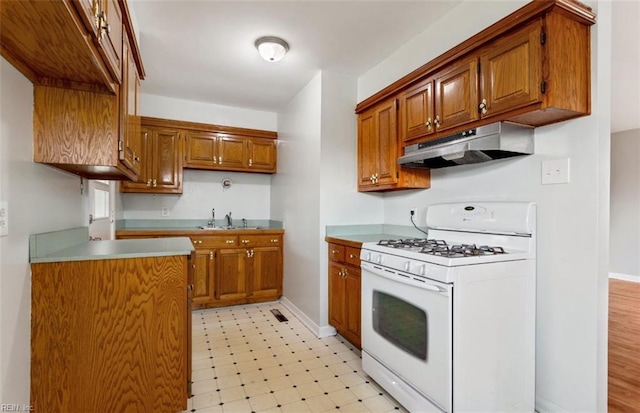 kitchen featuring white gas stove, under cabinet range hood, a sink, brown cabinets, and light floors