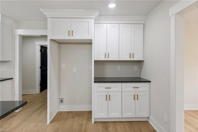 kitchen with light wood-style floors, baseboards, white cabinets, and dark stone countertops