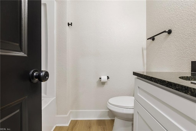 bathroom with a textured wall, toilet, wood finished floors, vanity, and baseboards