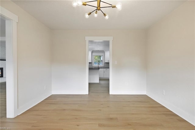 spare room featuring light wood-style floors, a chandelier, and baseboards