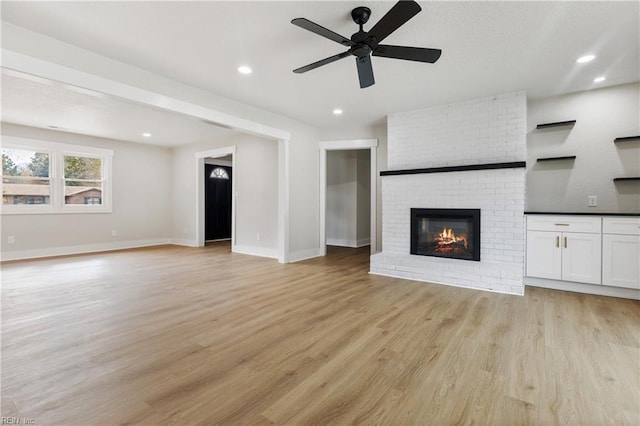 unfurnished living room featuring baseboards, a brick fireplace, recessed lighting, and light wood-style floors