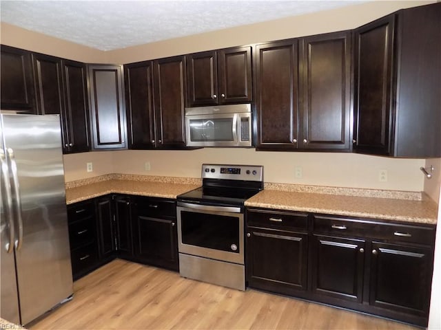 kitchen with appliances with stainless steel finishes, light countertops, light wood-style floors, and a textured ceiling