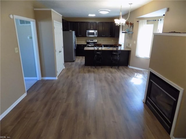 kitchen with a peninsula, a breakfast bar, dark wood-style flooring, baseboards, and appliances with stainless steel finishes