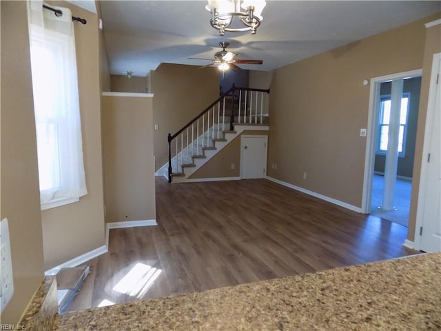 unfurnished living room featuring ceiling fan with notable chandelier, stairway, wood finished floors, and baseboards