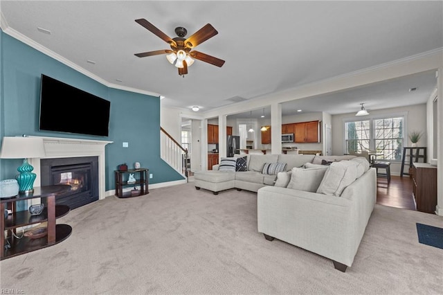 living area with light carpet, baseboards, stairs, ornamental molding, and a glass covered fireplace