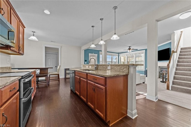 kitchen featuring dark wood-style floors, brown cabinets, light stone countertops, stainless steel appliances, and a sink