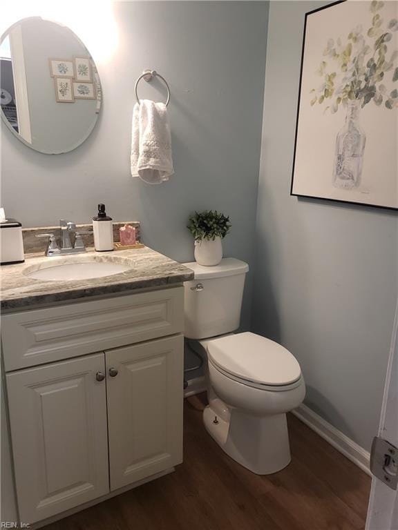 half bathroom with toilet, wood finished floors, vanity, and baseboards