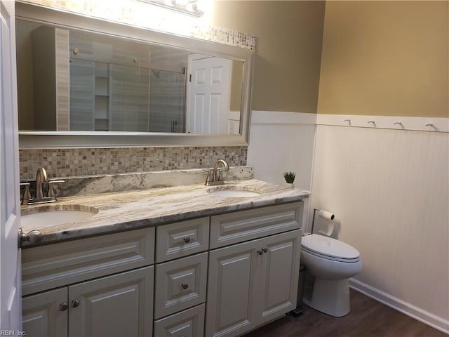 full bathroom with a wainscoted wall, a stall shower, a sink, and toilet