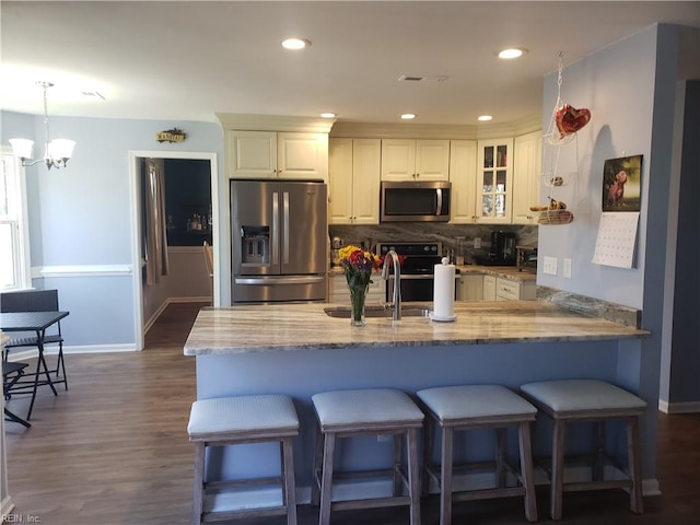 kitchen with a breakfast bar area, a sink, appliances with stainless steel finishes, backsplash, and light stone countertops