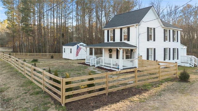 view of front facade featuring a storage shed, a fenced front yard, roof with shingles, an outdoor structure, and a porch