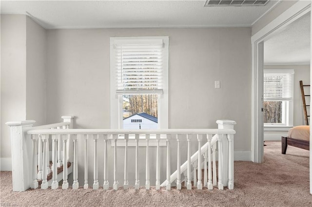 hallway featuring baseboards, visible vents, an upstairs landing, a textured ceiling, and carpet flooring