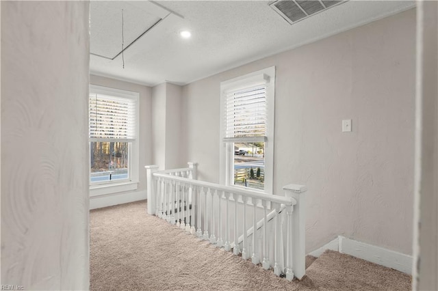 hallway featuring visible vents, attic access, carpet flooring, a textured ceiling, and an upstairs landing