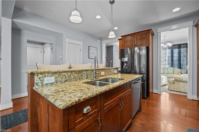 kitchen with a kitchen island with sink, wood finished floors, a sink, hanging light fixtures, and appliances with stainless steel finishes